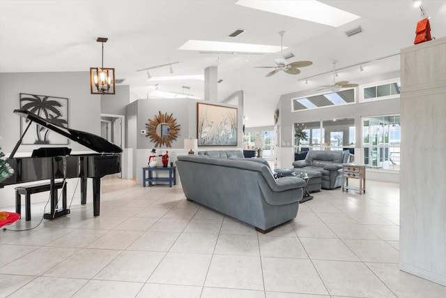 tiled living room with ceiling fan with notable chandelier, a skylight, high vaulted ceiling, and track lighting