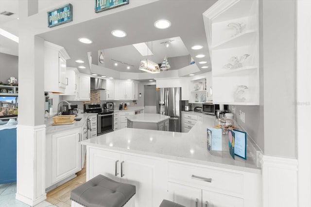 kitchen featuring kitchen peninsula, appliances with stainless steel finishes, light stone countertops, wall chimney range hood, and white cabinetry