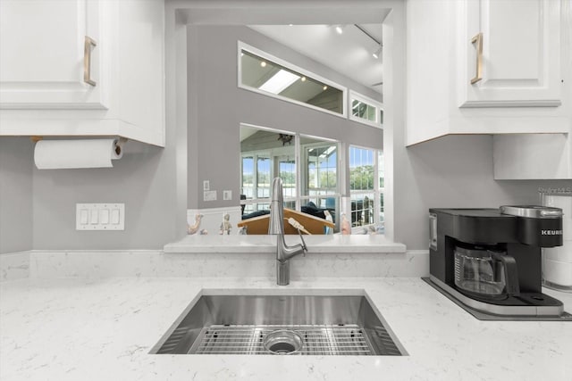 kitchen featuring white cabinets, light stone countertops, sink, and track lighting