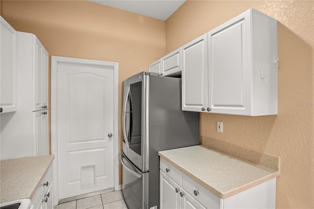 kitchen featuring white range oven, stainless steel refrigerator, white cabinets, and light tile patterned floors