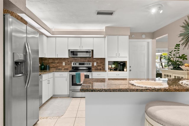 kitchen featuring backsplash, dark stone counters, stainless steel appliances, white cabinetry, and light tile patterned flooring