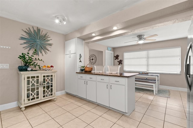 kitchen with kitchen peninsula, ceiling fan, dark stone countertops, white cabinetry, and light tile patterned flooring