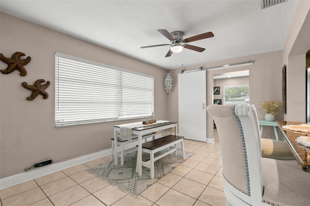 dining area featuring ceiling fan, light tile patterned flooring, a barn door, and a textured ceiling