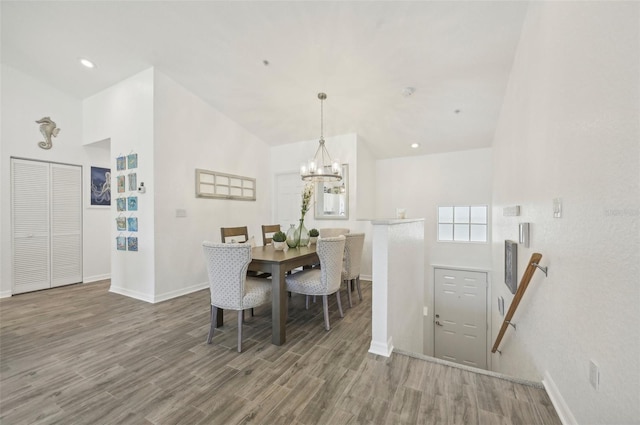 dining space with wood-type flooring, an inviting chandelier, and lofted ceiling