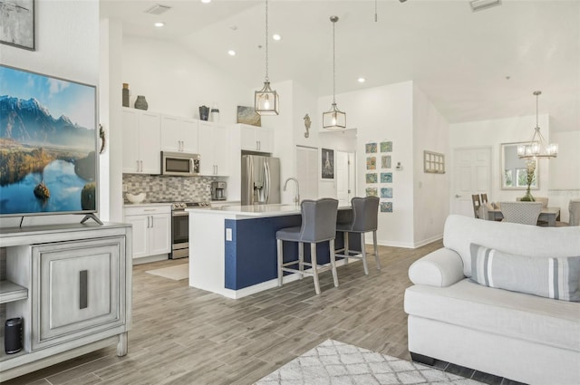 kitchen featuring a center island with sink, white cabinets, stainless steel appliances, and decorative light fixtures