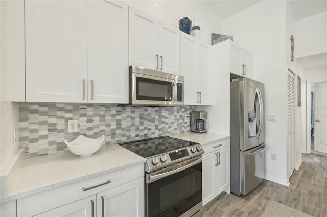 kitchen with white cabinets, light hardwood / wood-style flooring, decorative backsplash, light stone counters, and stainless steel appliances