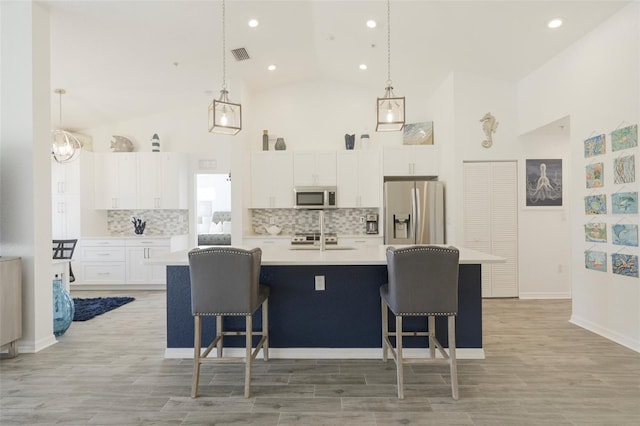 kitchen with appliances with stainless steel finishes, decorative light fixtures, a kitchen island with sink, white cabinets, and light wood-type flooring