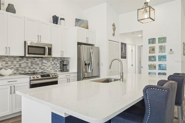 kitchen featuring hanging light fixtures, appliances with stainless steel finishes, white cabinetry, and a kitchen island with sink