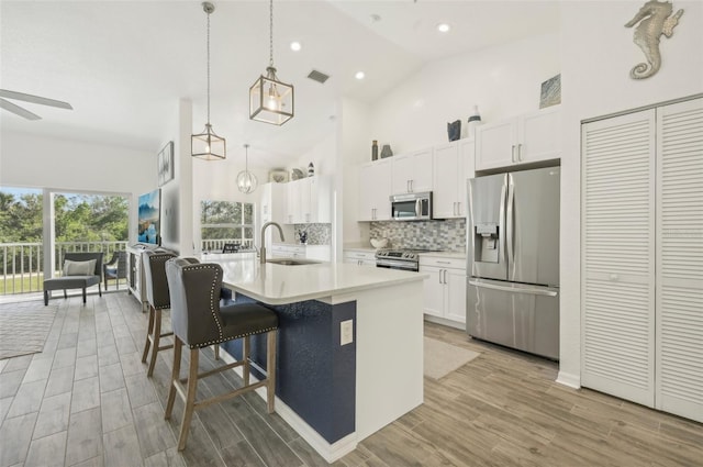 kitchen featuring stainless steel appliances, sink, decorative light fixtures, white cabinets, and an island with sink