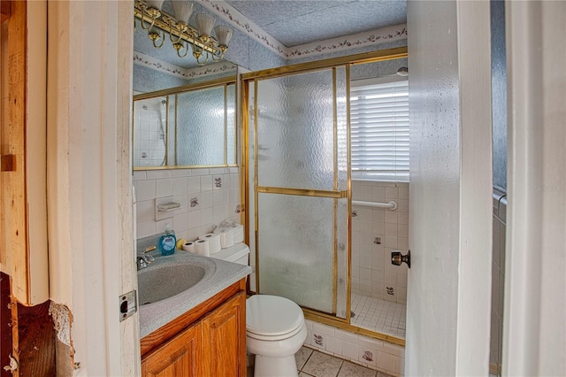 bathroom with tile patterned floors, toilet, a shower with door, vanity, and tile walls