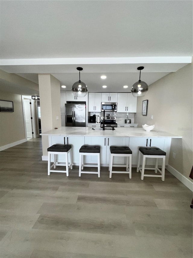 kitchen featuring kitchen peninsula, stainless steel appliances, white cabinetry, and hanging light fixtures