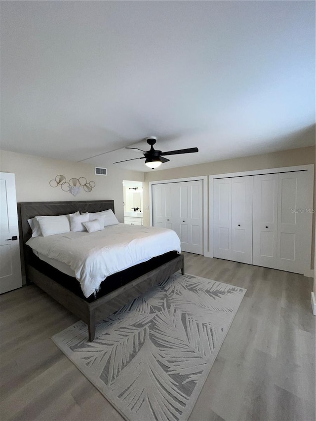 bedroom with ceiling fan, light wood-type flooring, and two closets