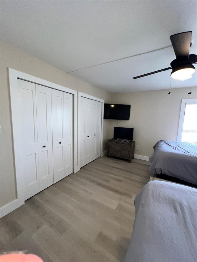 bedroom featuring ceiling fan, two closets, and light hardwood / wood-style flooring