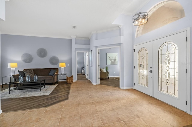 foyer entrance with a notable chandelier, light hardwood / wood-style floors, crown molding, and french doors