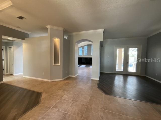 empty room featuring ornamental molding, arched walkways, light tile patterned floors, and french doors