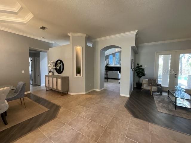interior space with light tile patterned floors, visible vents, arched walkways, ornamental molding, and french doors