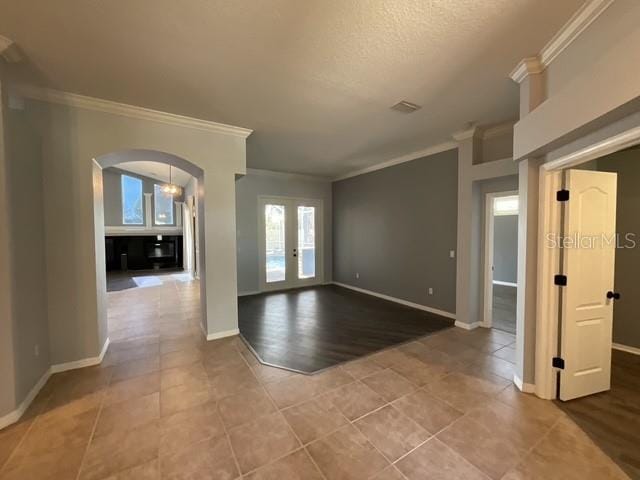 empty room featuring baseboards, arched walkways, ornamental molding, french doors, and tile patterned flooring