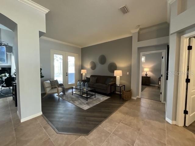 living area featuring light tile patterned floors, visible vents, baseboards, ornamental molding, and french doors
