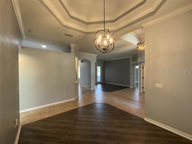 empty room with arched walkways, wood finished floors, a notable chandelier, crown molding, and a tray ceiling