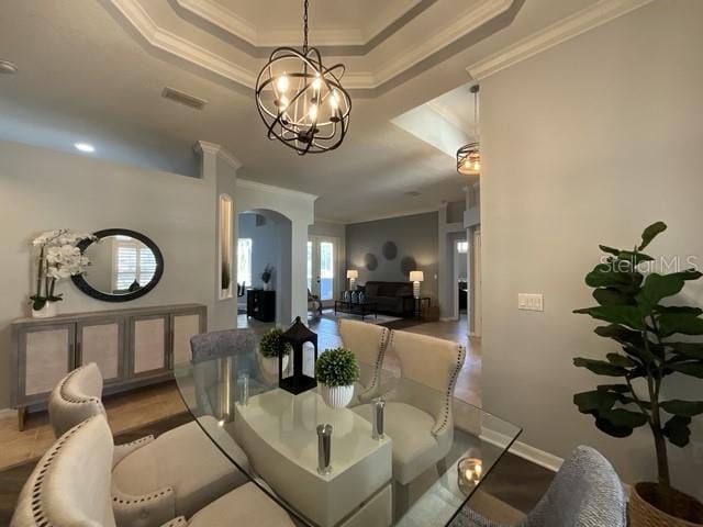 dining area with crown molding, a chandelier, a tray ceiling, arched walkways, and baseboards