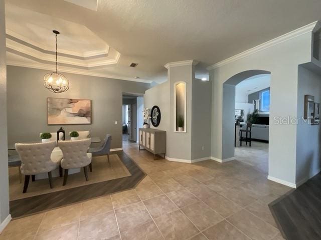 tiled dining space with a notable chandelier, a tray ceiling, baseboards, ornamental molding, and arched walkways