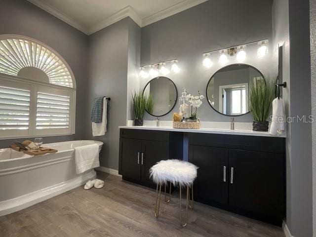 full bath featuring a bath, crown molding, double vanity, baseboards, and wood finished floors