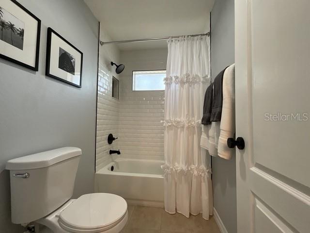 full bath with tile patterned floors, shower / bathtub combination with curtain, and toilet