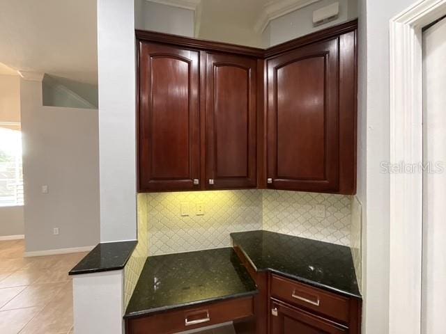 kitchen featuring dark stone counters, decorative backsplash, light tile patterned floors, baseboards, and dark brown cabinets