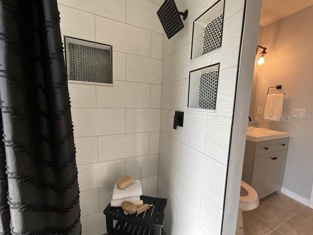 bathroom with vanity, baseboards, tile patterned flooring, and tiled shower