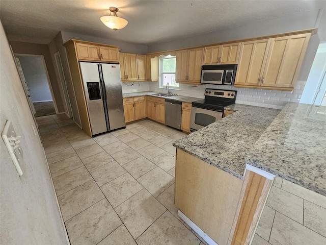 kitchen featuring light stone countertops, decorative backsplash, kitchen peninsula, stainless steel appliances, and sink