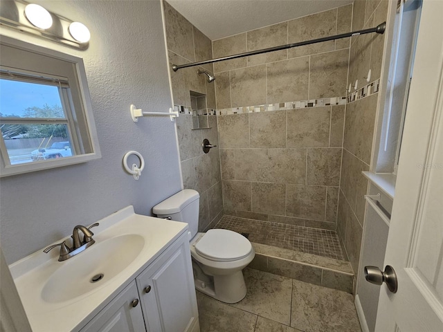 bathroom featuring a tile shower, vanity, and toilet