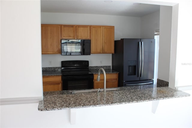 kitchen with dark stone counters, black appliances, a kitchen breakfast bar, sink, and kitchen peninsula