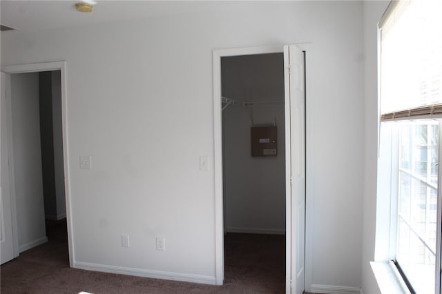 unfurnished bedroom with a walk in closet, a closet, multiple windows, and dark colored carpet