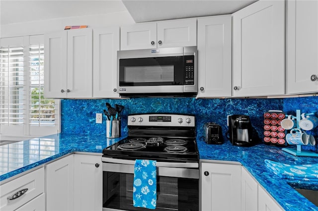 kitchen featuring white cabinets, backsplash, stainless steel appliances, and dark stone countertops