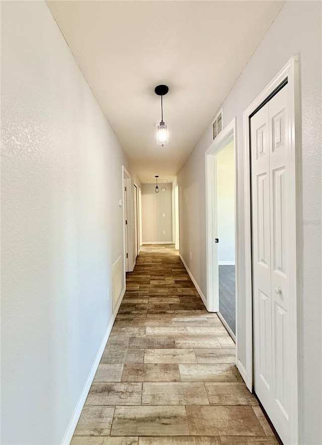 hallway featuring visible vents, light wood-type flooring, and baseboards