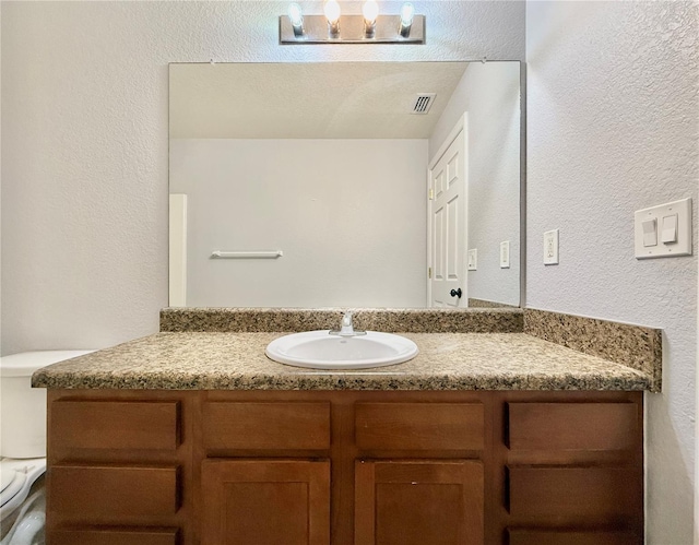 bathroom featuring an inviting chandelier, vanity, visible vents, toilet, and a textured wall