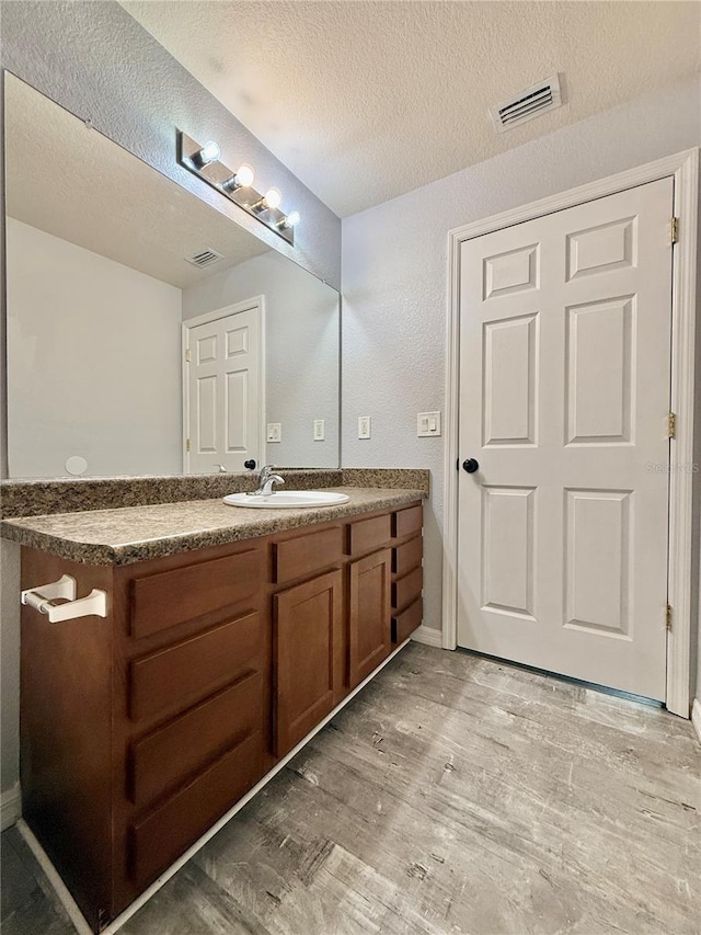 bathroom with a textured ceiling, wood finished floors, vanity, and visible vents
