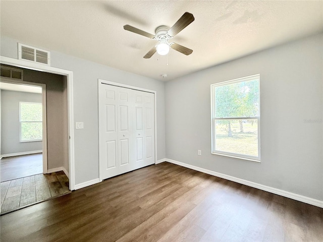 unfurnished bedroom featuring visible vents, multiple windows, baseboards, and dark wood-style floors