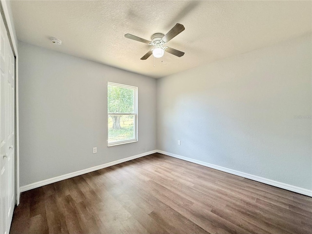 unfurnished room with ceiling fan, a textured ceiling, baseboards, and dark wood-style floors