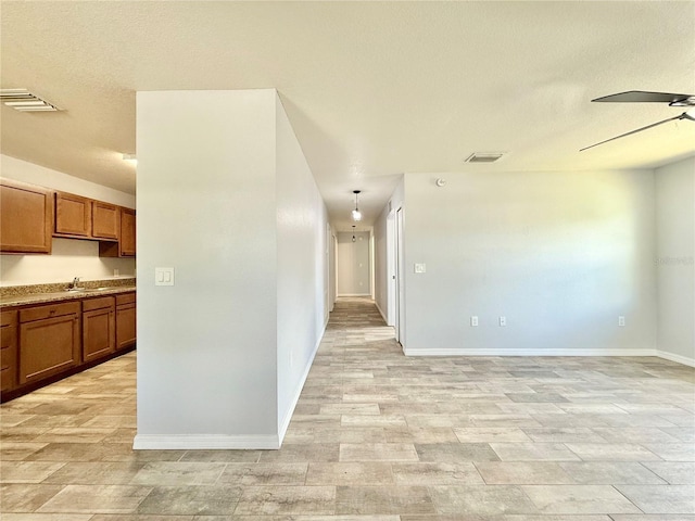 spare room featuring a textured ceiling, a ceiling fan, visible vents, a sink, and baseboards