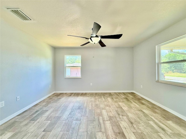 empty room featuring light wood finished floors, baseboards, a ceiling fan, and visible vents