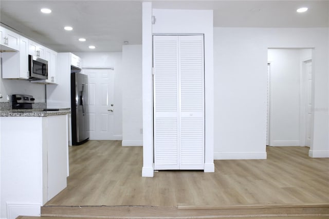 kitchen featuring white cabinets, appliances with stainless steel finishes, light hardwood / wood-style flooring, and dark stone countertops