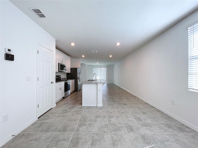 kitchen with a kitchen island with sink, white cabinets, sink, light tile patterned floors, and stainless steel appliances