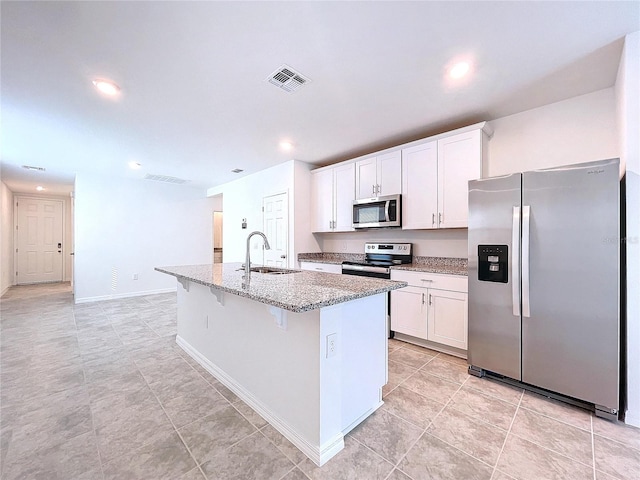 kitchen featuring white cabinets, light stone countertops, stainless steel appliances, and a kitchen island with sink