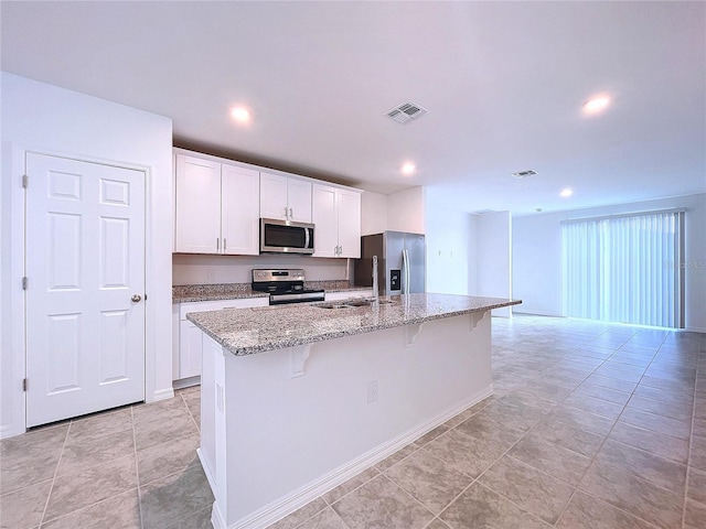 kitchen featuring a kitchen bar, light stone counters, stainless steel appliances, white cabinets, and an island with sink