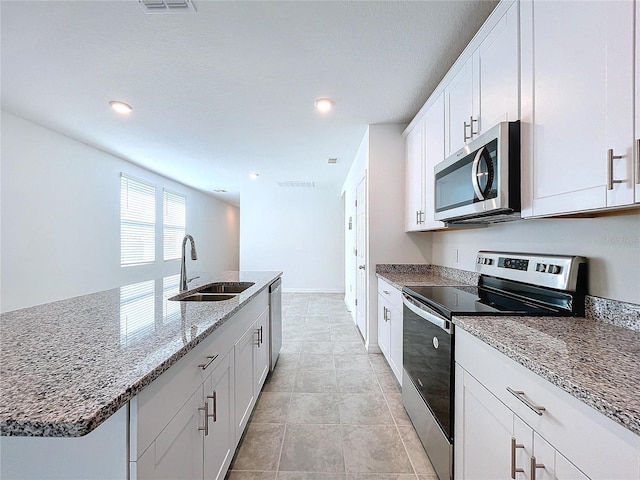 kitchen with light stone countertops, sink, a center island with sink, white cabinets, and appliances with stainless steel finishes