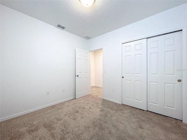 unfurnished bedroom featuring a textured ceiling, light carpet, and a closet