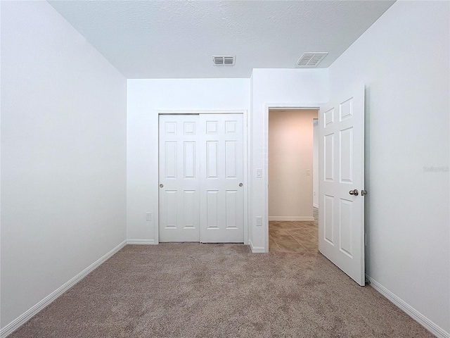 unfurnished bedroom featuring a textured ceiling, light colored carpet, and a closet