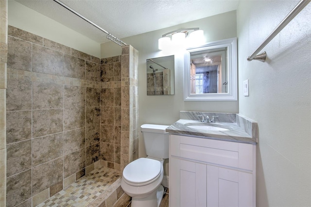 bathroom with vanity, toilet, a textured ceiling, and a tile shower