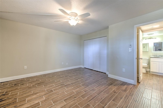 unfurnished bedroom featuring wood-type flooring, a textured ceiling, ensuite bath, and ceiling fan